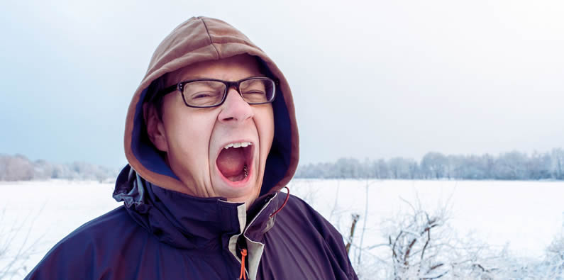 Mann gähnt vor Wintermüdigkeit im Schnee